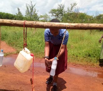 Hvordan man vasker hendene på skolen, en flaske med såpe og en kanne med vann. Men tråkker på pinnen, som gjør at kannen med vann heller ut litt vann så man får skylt hendene sine