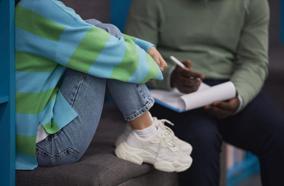 Ungdom sitter i en sofa med en voksen behandler ved siden av