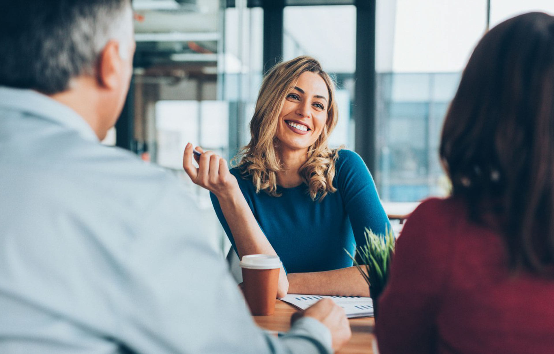 Kvinne i møte med to andre kollegaer, smiler og prater sammen.