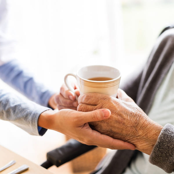 Hjelpepleier som serverer te til eldre kvinne