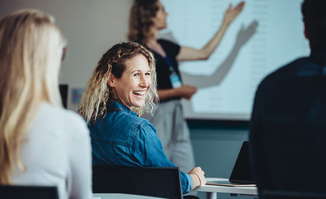 Person sitter i klasserom og smiler