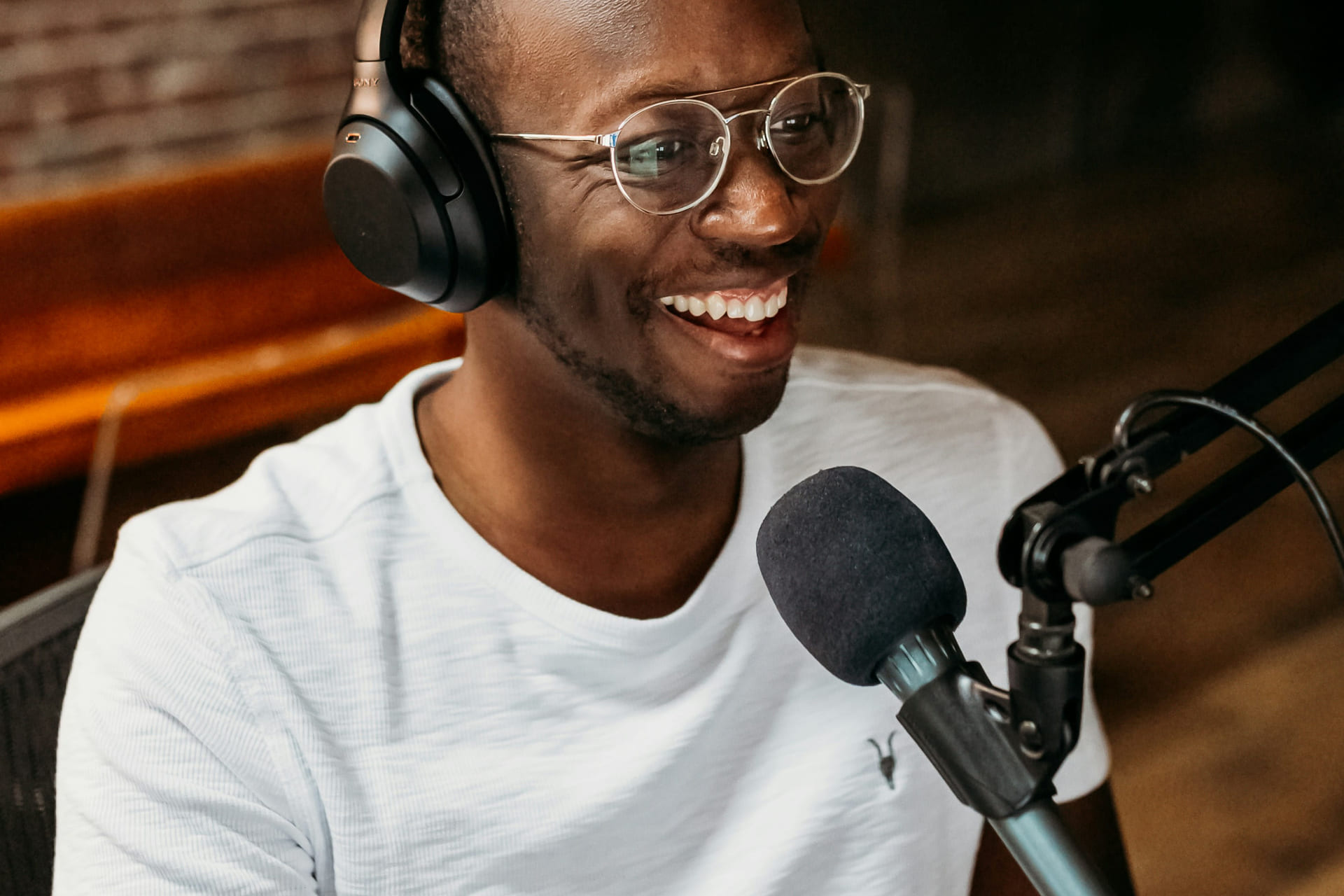 Mann med hvit t-skjorte og briller som har på headset og snakker inn i en mikrofon