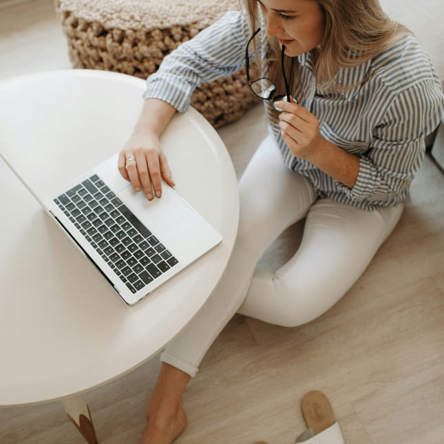 Kvinne sitter på gulvet og ser på en macbook